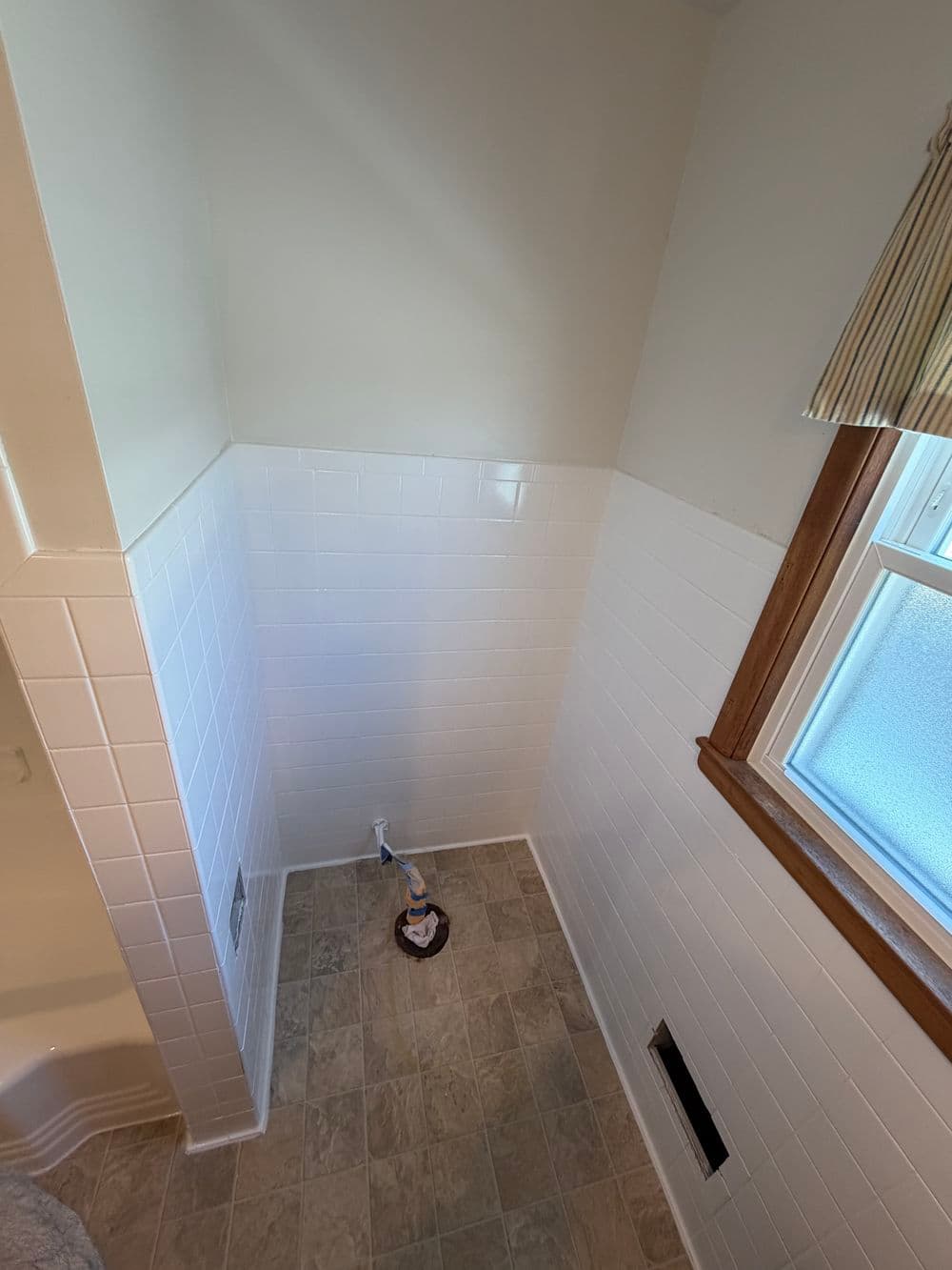 Bright bathroom corner with white tile walls and a window, showcasing clean, modern design.