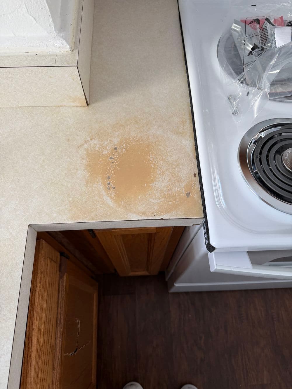 Stained kitchen countertop near a stove, showing discoloration and wear.