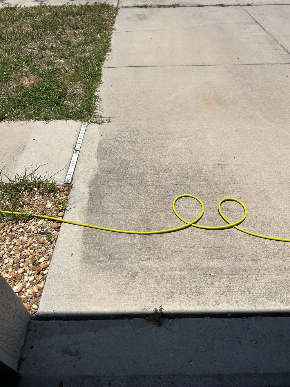 Yellow extension cord on a concrete driveway with grass and gravel at the edge.