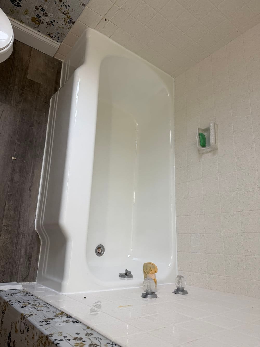 Empty white bathtub in a bathroom with a wooden floor and wallpapered accents.