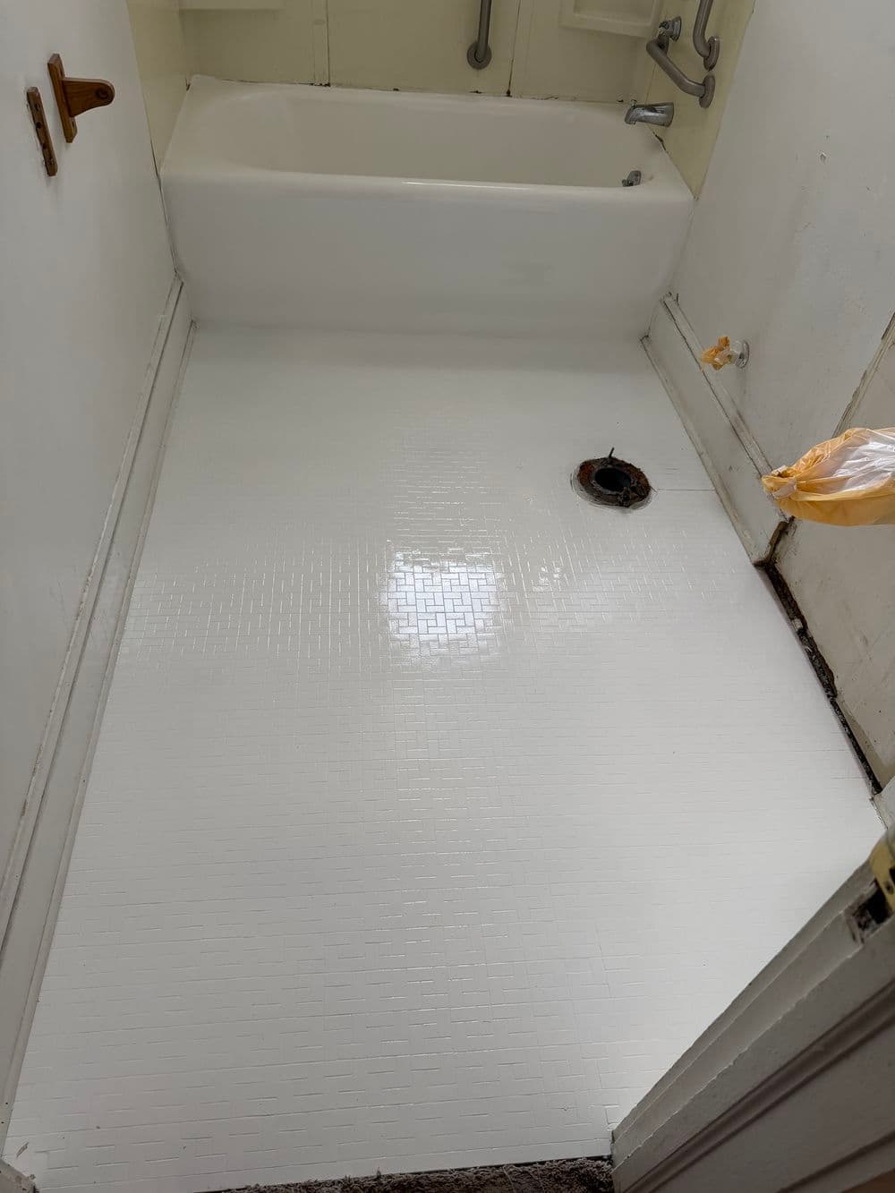 White bathroom floor with a bathtub, drain, and unfinished walls awaiting renovation.
