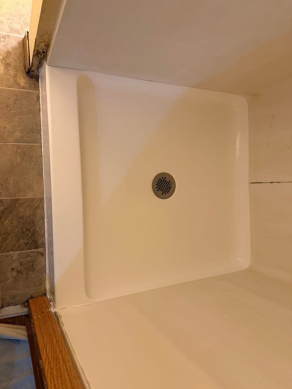 Clean shower base with drain, featuring a smooth white surface and corner installation.