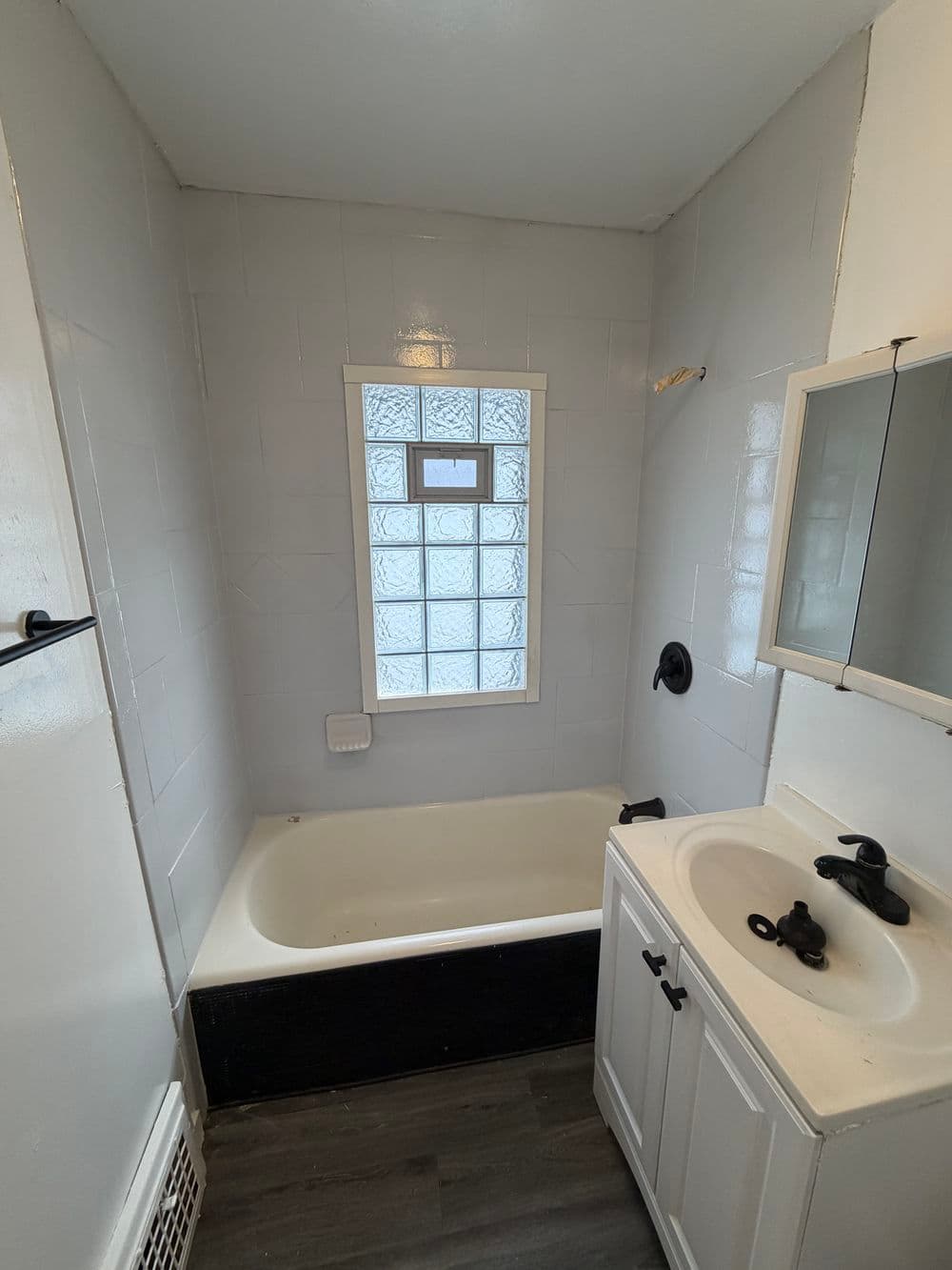 Compact bathroom with a tub, glass block window, and modern sink vanity. Neutral colors.