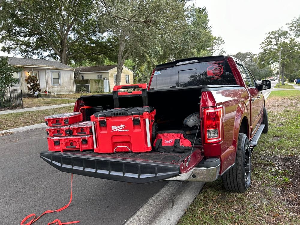Red pickup truck with open tailgate displaying Milwaukee toolboxes and equipment.