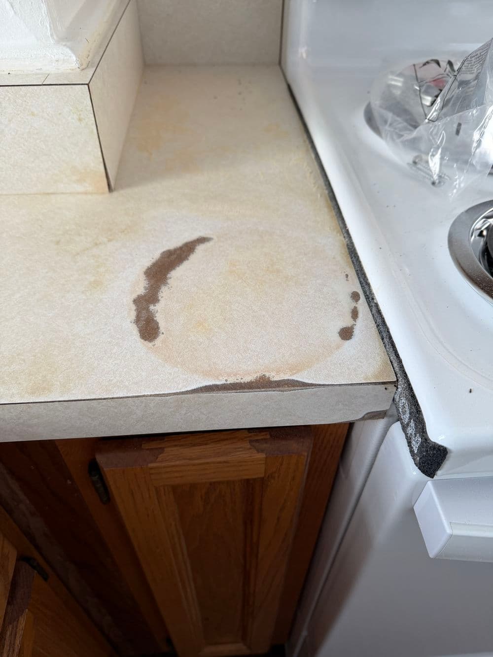 Stained kitchen countertop with water marks and discoloration near the stove area.