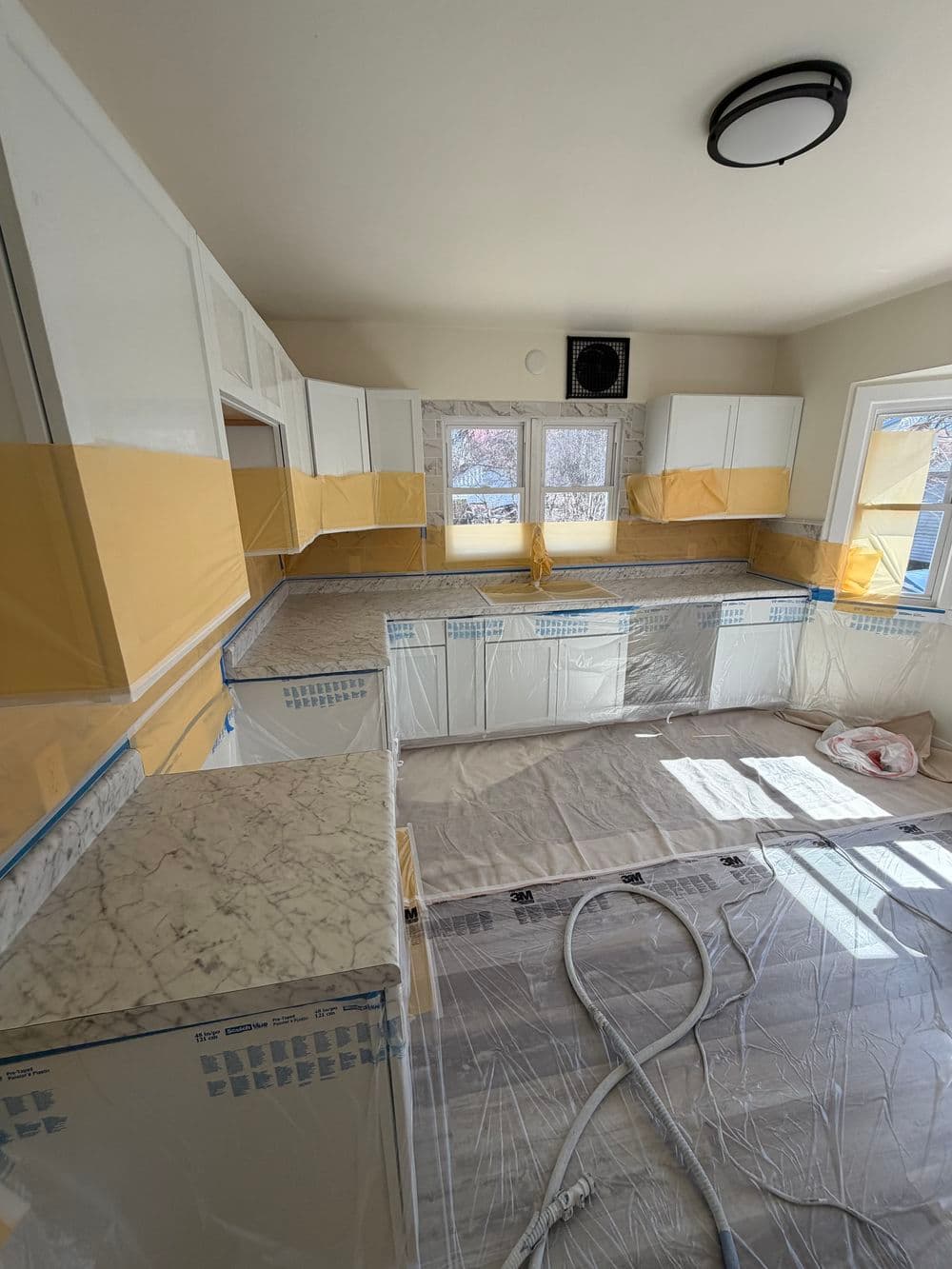 Renovated kitchen with white cabinets, marble countertops, and protective plastic coverings.