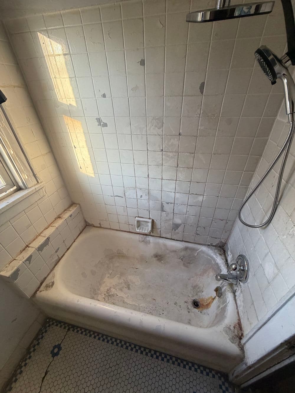 Dirty bathtub with stained tiles and a handheld showerhead in a neglected bathroom.