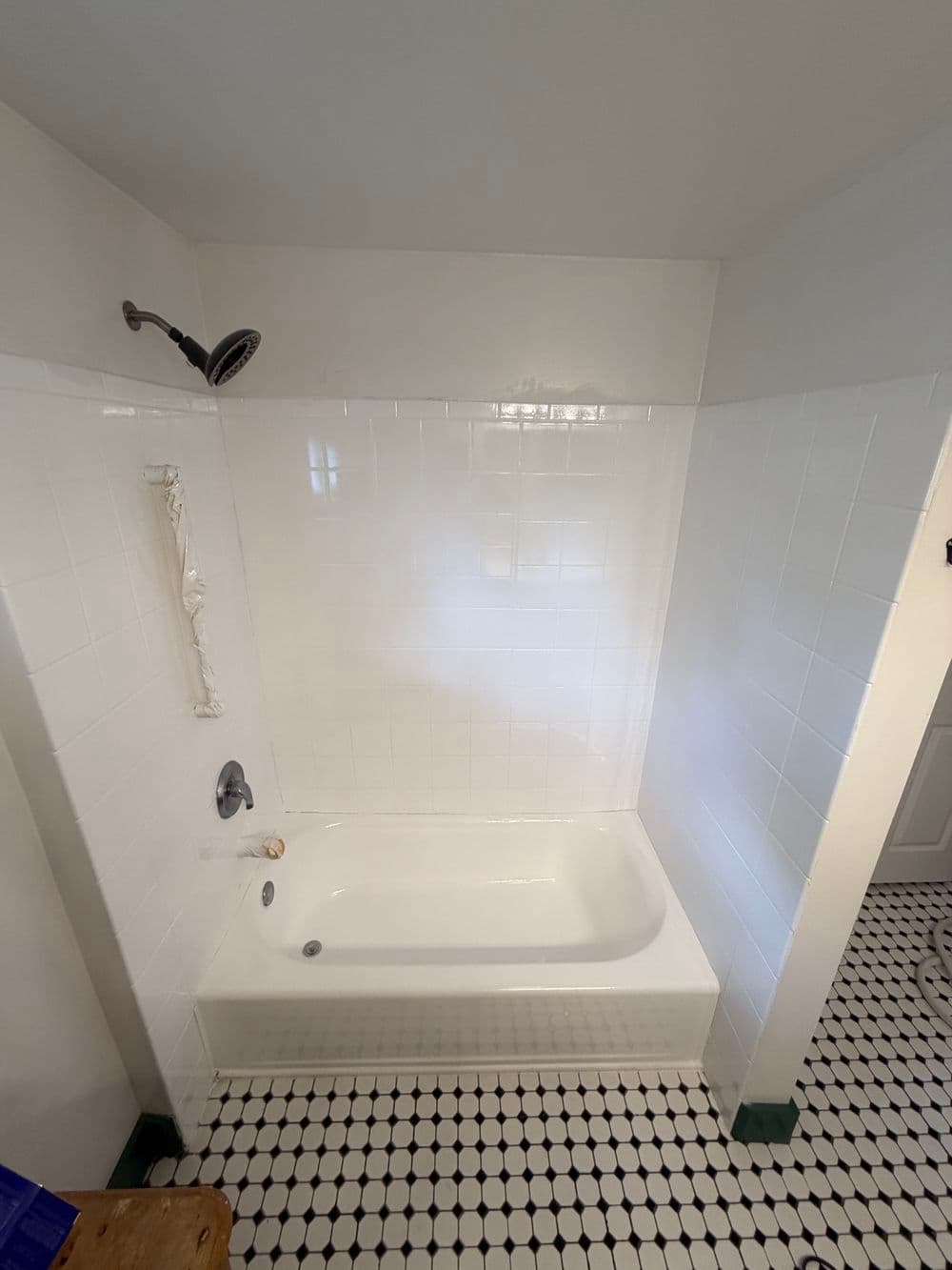 Bright bathroom featuring a white tub, showerhead, and classic black-and-white tiled floor.