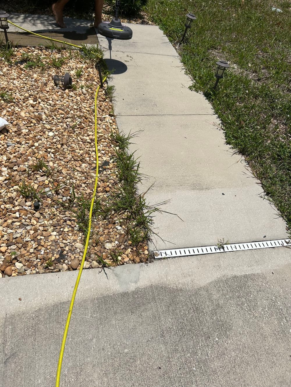 Power washing a concrete pathway alongside gravel landscaping and grass.