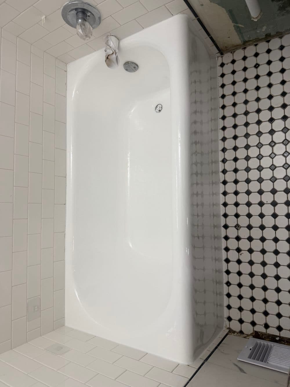 Modern white bathtub on tiled floor with black and white hexagonal pattern.