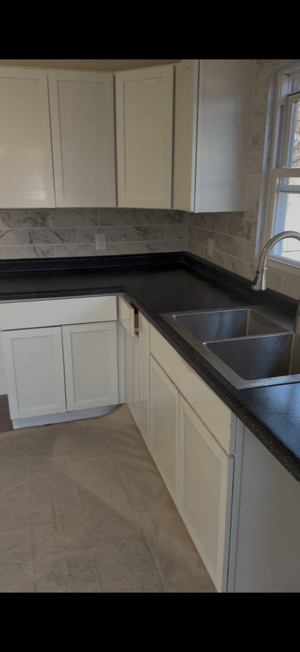 Modern kitchen with white cabinetry, black countertops, and double sink under a window.
