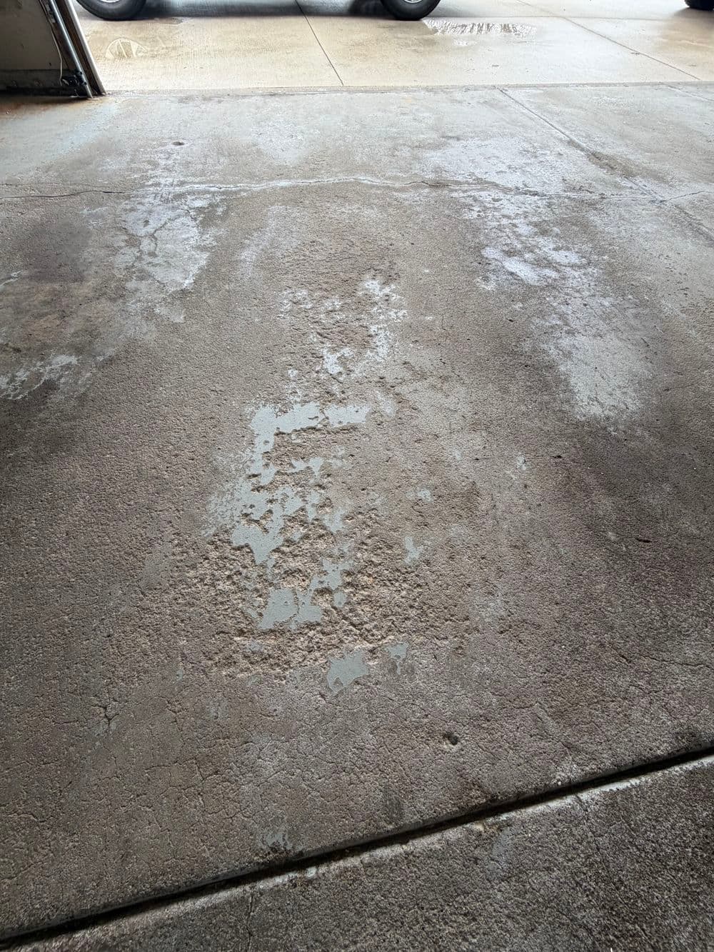Wet concrete surface with visible stains and peeling paint in a garage setting.