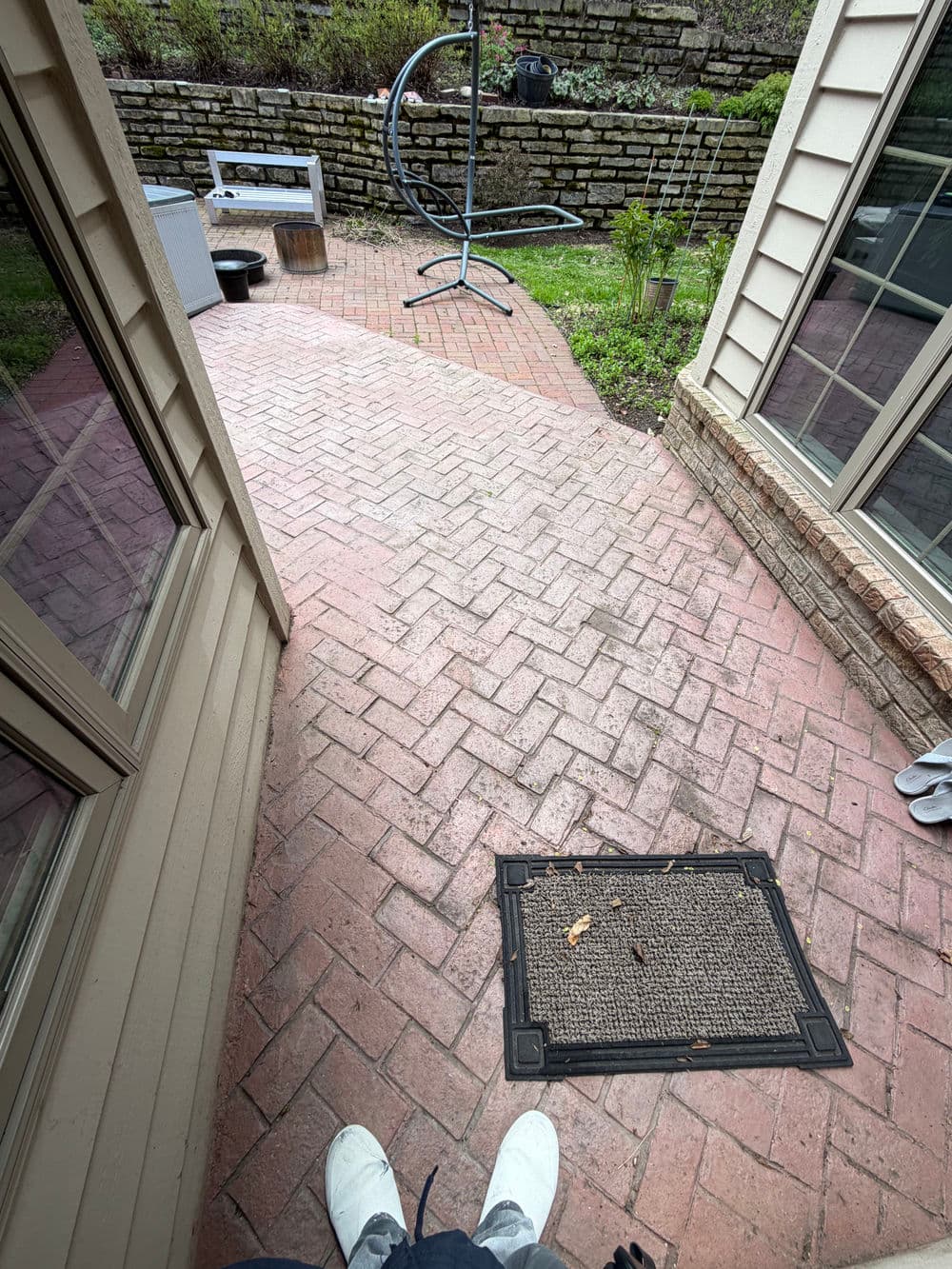 Brick walkway leading to a patio area with outdoor furniture and greenery.