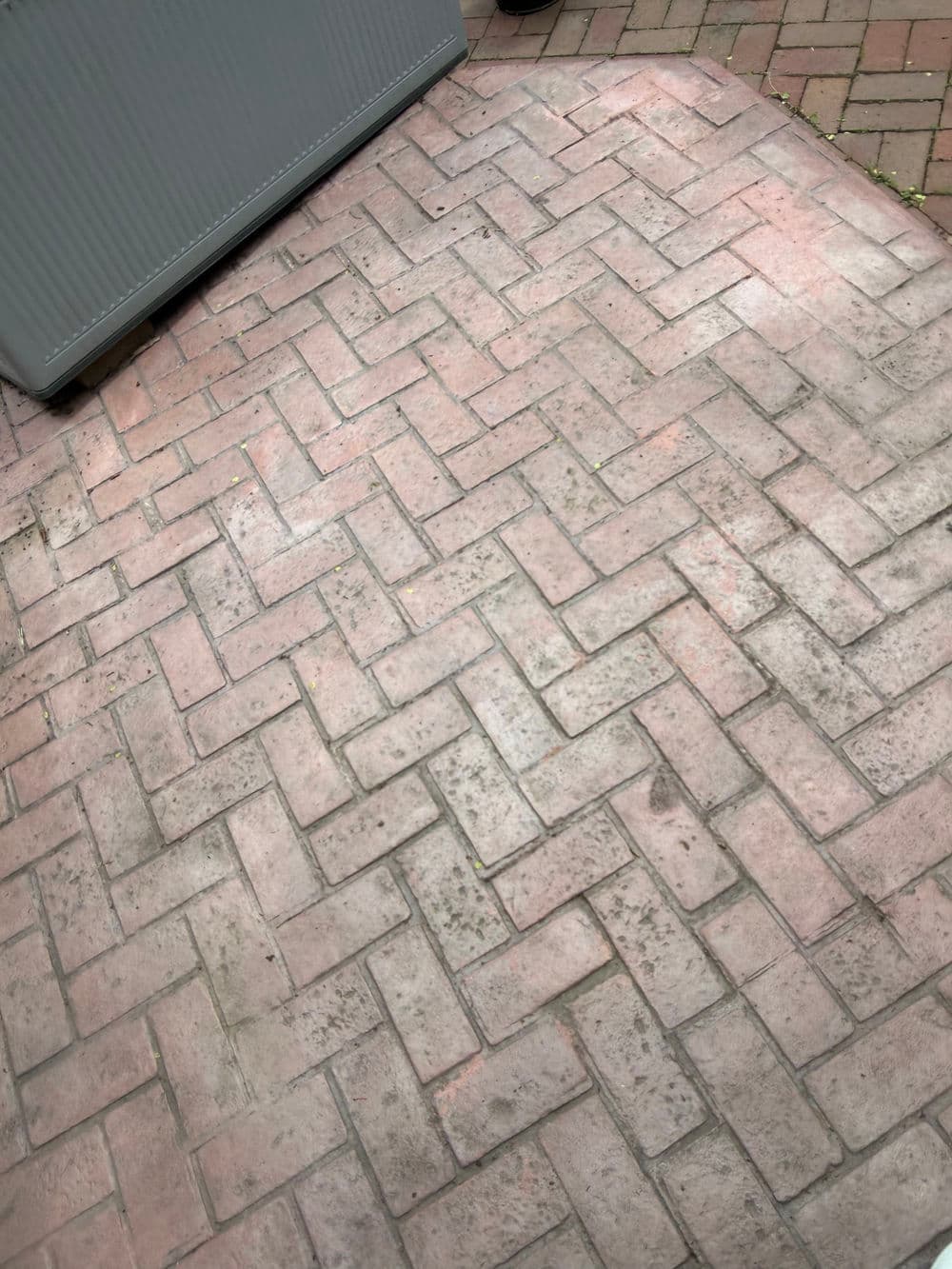 Patterned red brick patio surface with a clean, modern design and gray storage box in background.