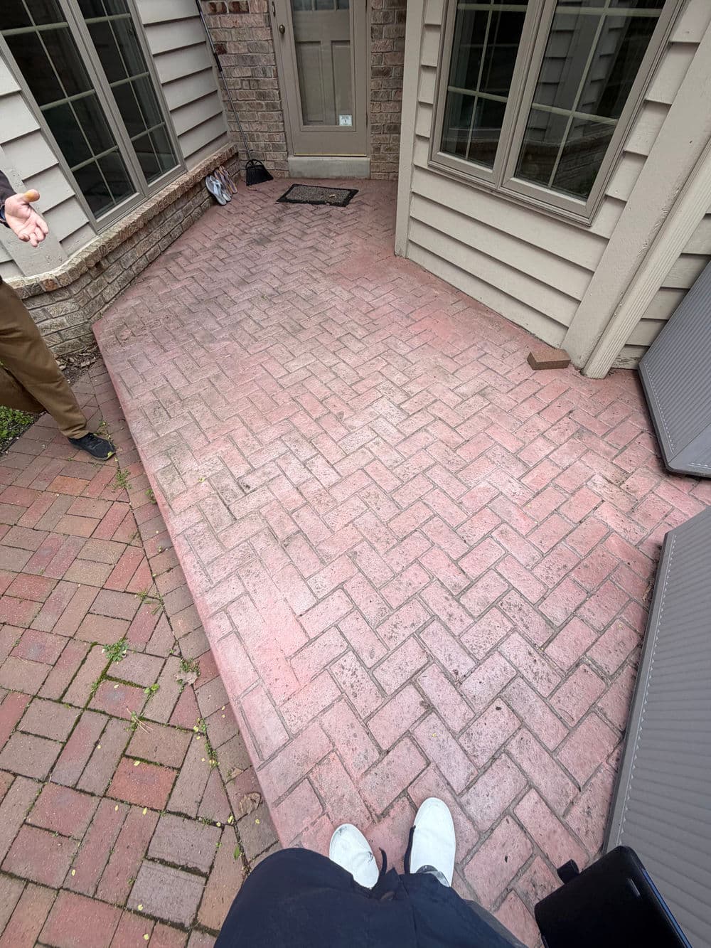 Brick patio in residential area, showing clean pavers and adjacent entryway with person gesturing.