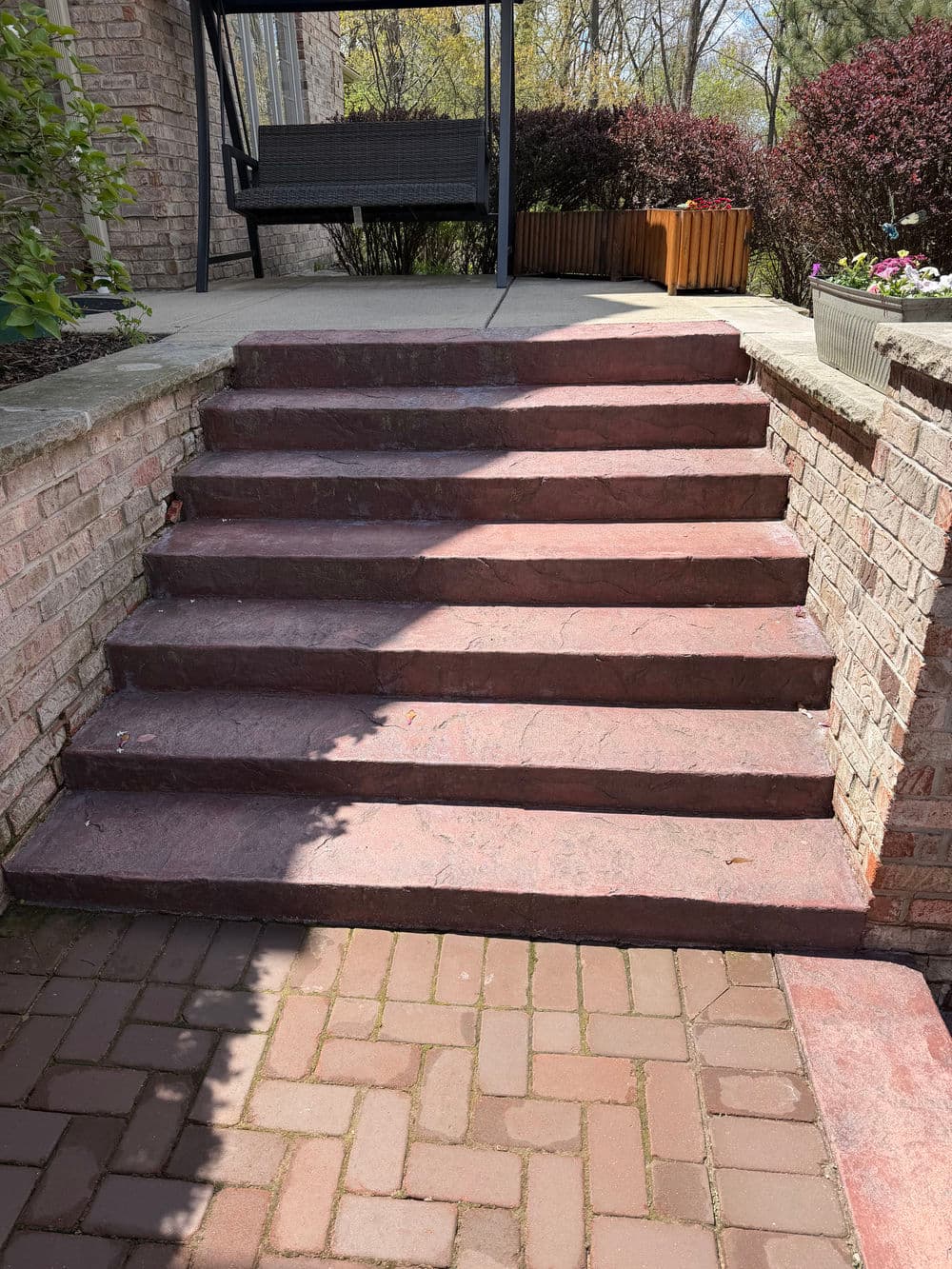 Red stone steps leading to a porch, surrounded by greenery and flower planters.